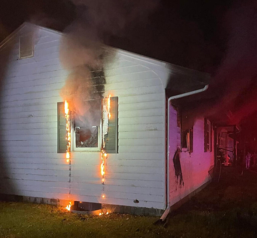 Smoke & flames pour from the side windows of a Little Road home in Maynard early Tuesday morning. (Photo courtesy of Maynard Fire Department)