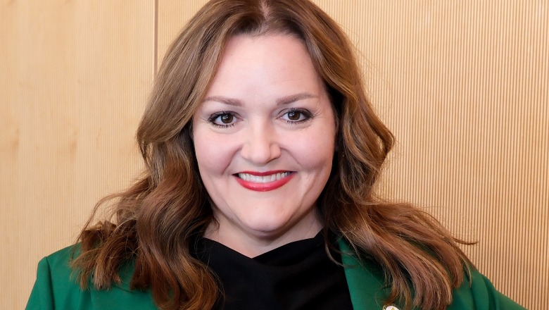 Dr. Sharon Hodge headshot. She has red hair is standing in front of a wall of wood paneling and is smiling.