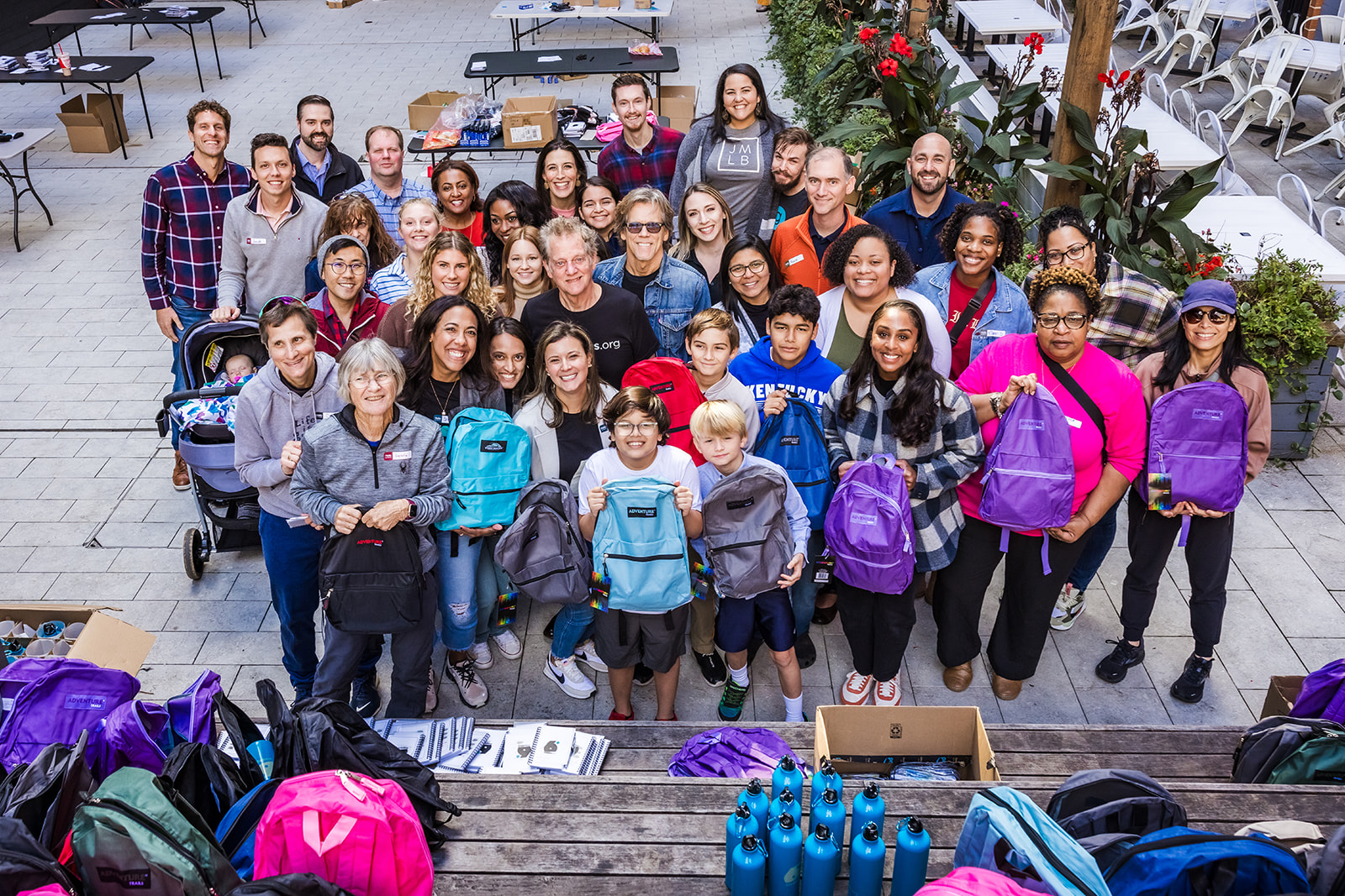 Actor Kevin Bacon and volunteers holding up completed resource kits in backpacks at a recent event.