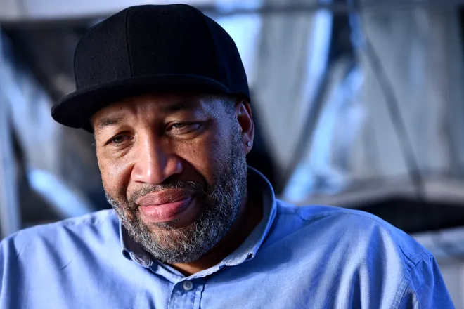 A picture of Charles Luster, the head of 2Gether We Eat. It's a portrait of him in a black hat from slightly above the waist up with a blue background.