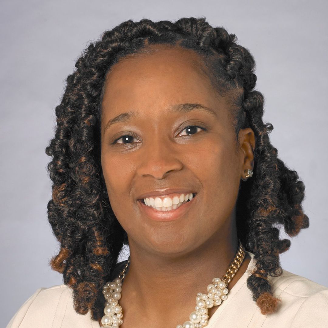 Portrait of LaTonia Monroe Naylor smiling in a cream-colored outfit with a detailed pearl necklace, her hair styled in twisted locks.