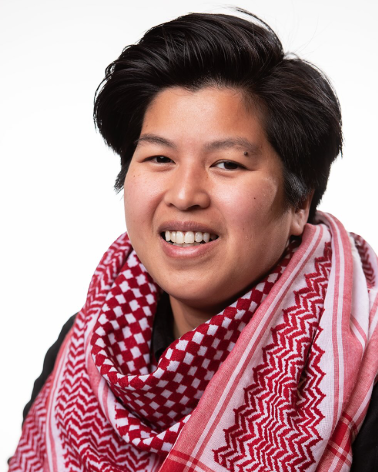 Portrait of a smiling nonbinary Asian individual wearing a red and white checkered scarf. They have short black hair and are looking directly at the camera with a warm, friendly expression.