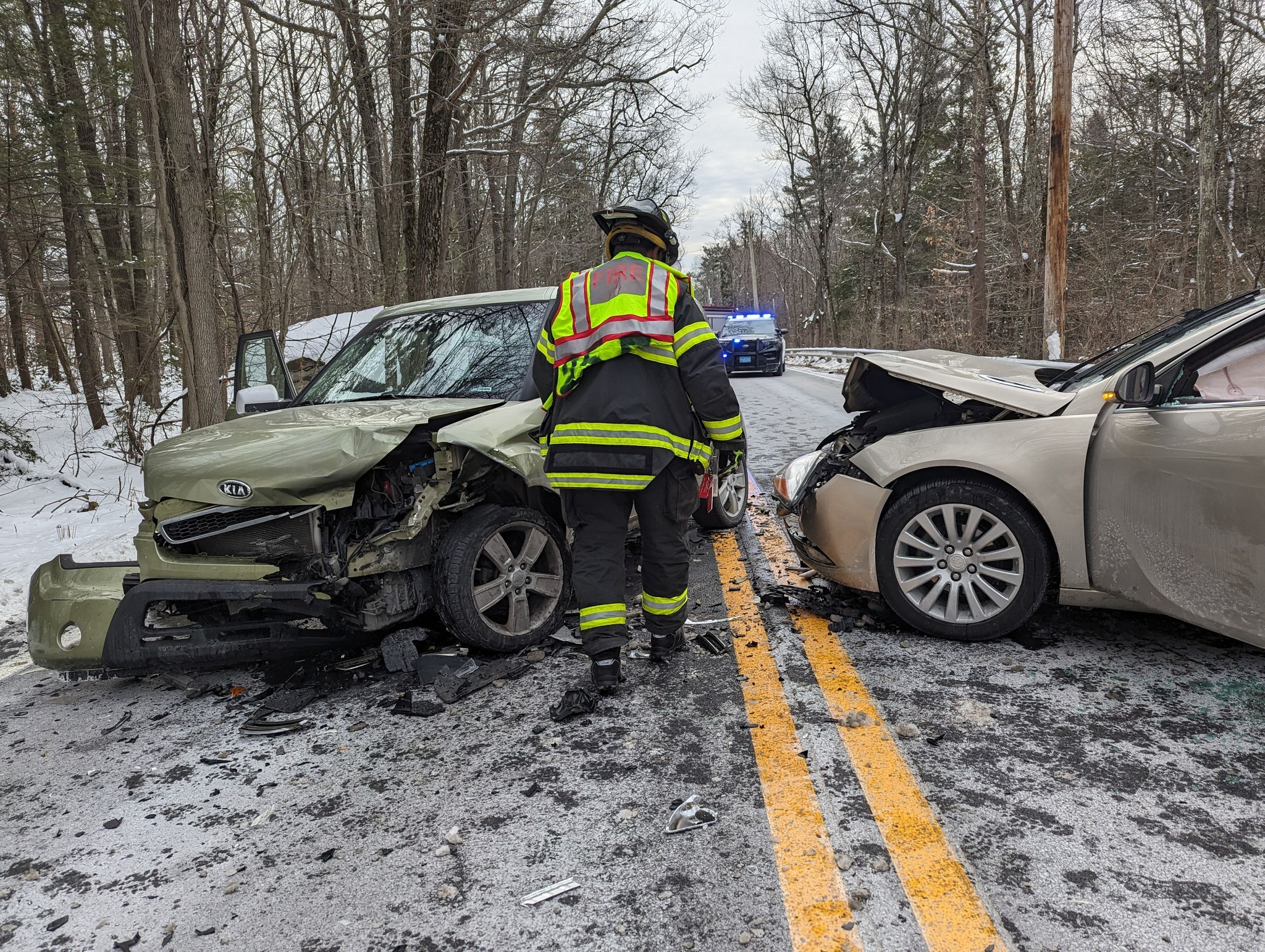 A firefighter stands between two vehicles involved in a head-on collision on Redemption Rock Trail (Route 140) in Princeton, Massachusetts, on January 23, 2025. The front ends of both vehicles are heavily damaged, and police lights are visible in the background. (Photo Credit: Princeton Fire Department)