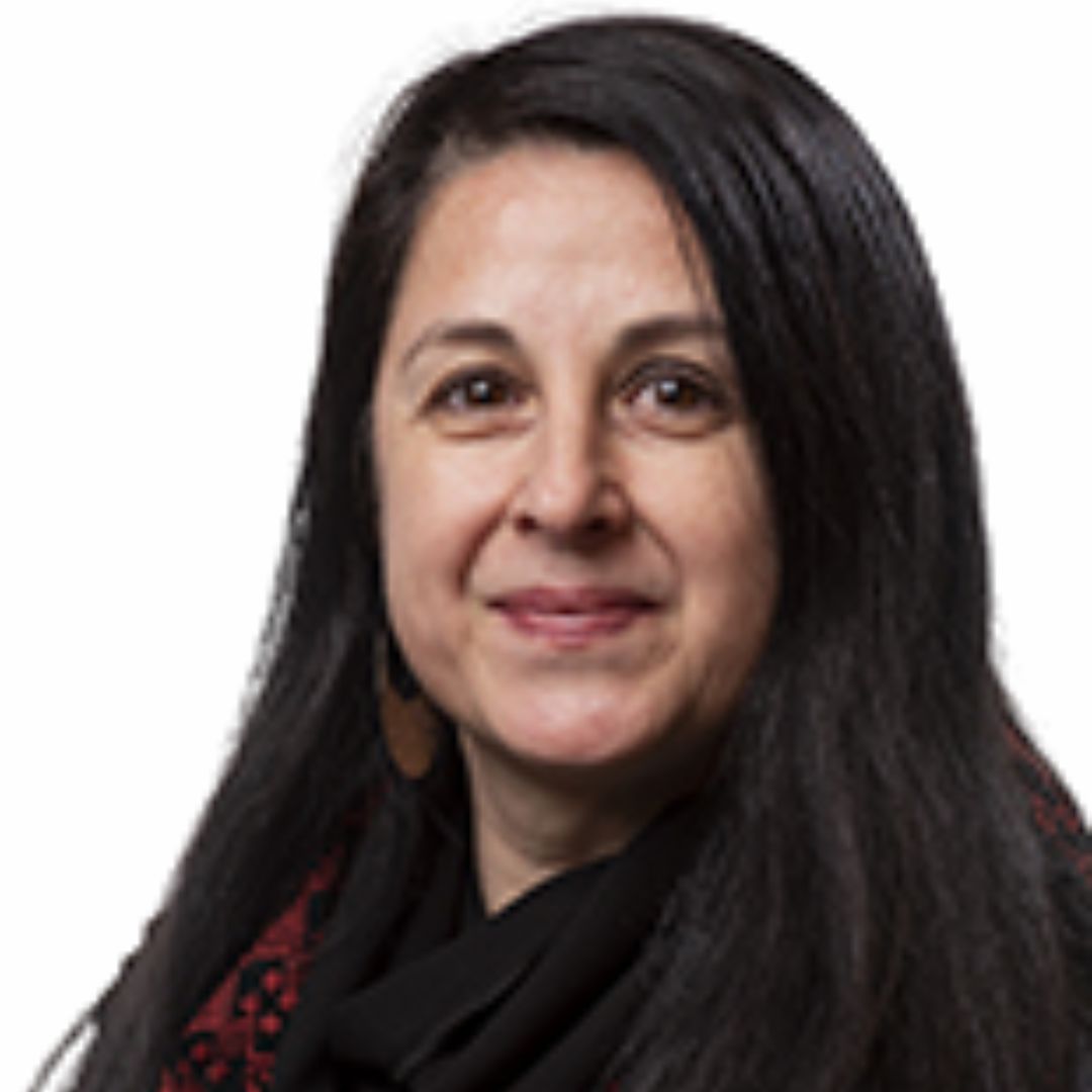 A woman with long, dark hair and a warm smile is pictured against a plain white background. She is wearing a black and red patterned scarf and dark clothing. Her expression is calm and approachable.