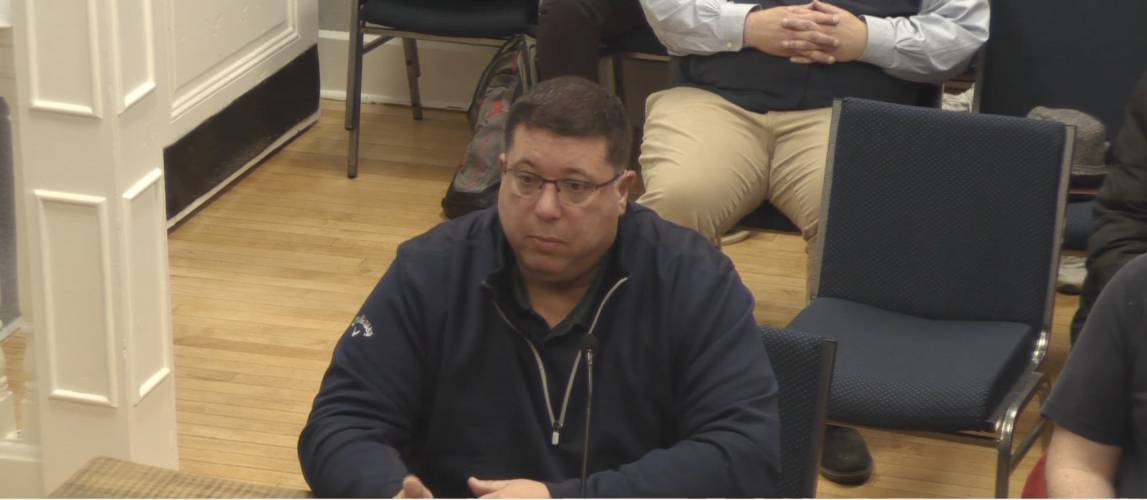 A screenshot showing Orange Police Chief James Sullivan, wearing a navy-blue jacket, speaking to the Selectboard about a fraud case that cost the town approximately $338,000. (Courtesy of Athol-Orange Community Television and The Athol Daily News)