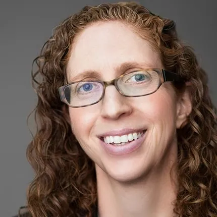 Headshot of Carolyn Jackson, CEO of Saint Vincent Hospital. She has curly reddish-brown hair, wears glasses, and is smiling while looking directly at the camera.