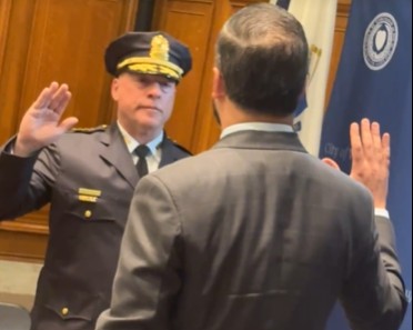 Paul B. Saucier, wearing a Worcester Police Department uniform and hat, raises his right hand as he is sworn in as the city's police chief by City Manager Eric D. Batista, who also raises his hand. The ceremony takes place inside a wood-paneled room with official flags in the background.