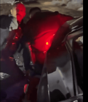 Screenshot showing two Shrewsbury police officers illuminated by red emergency lighting, forcibly detaining a man beside a vehicle at night