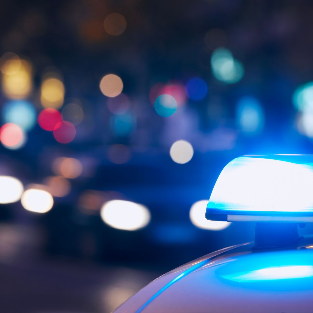 A close-up of a police car's flashing blue emergency lights at night, with blurred city traffic and streetlights in the background.