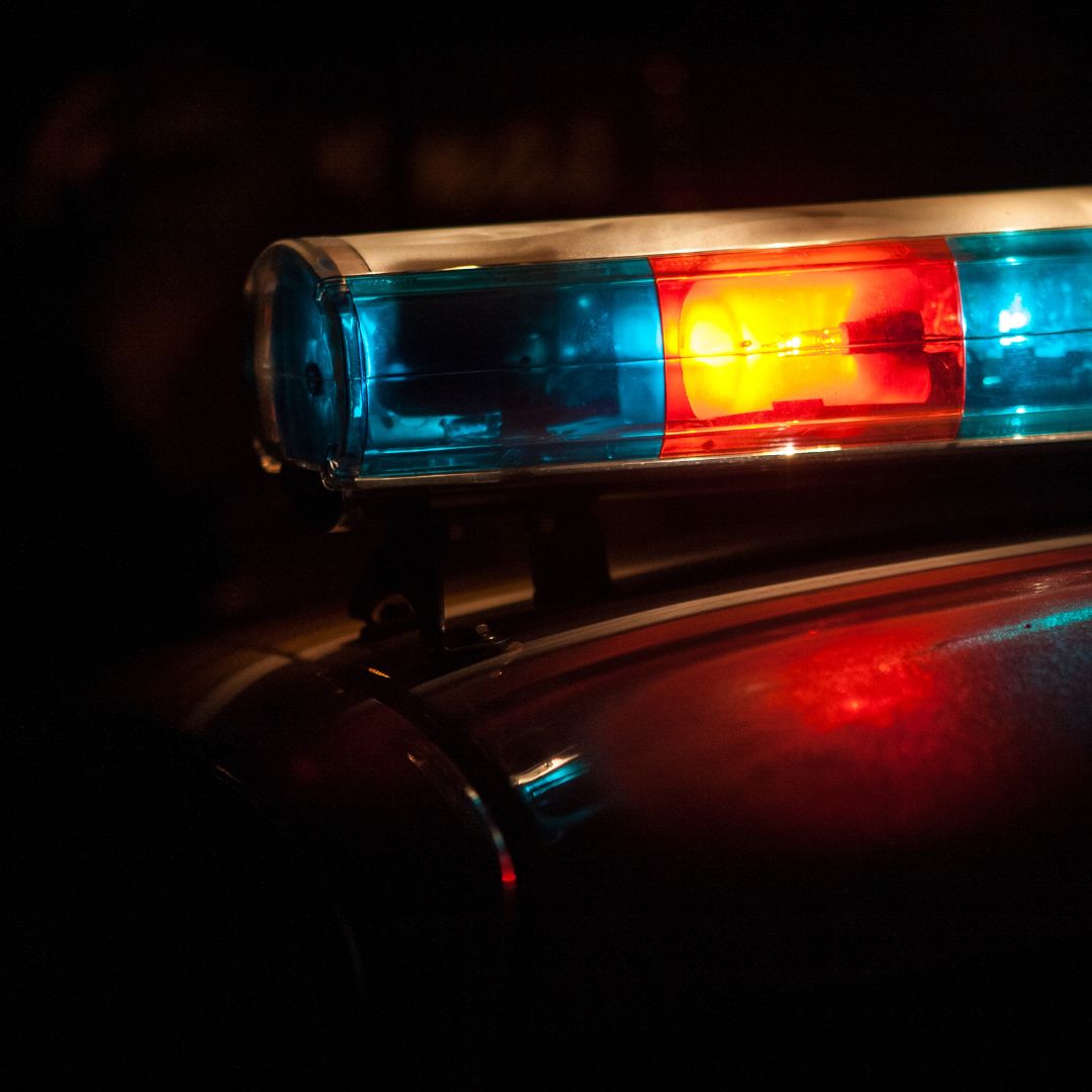 A close-up of a police car's emergency lights flashing red and blue in the dark, reflecting off the vehicle's surface.
