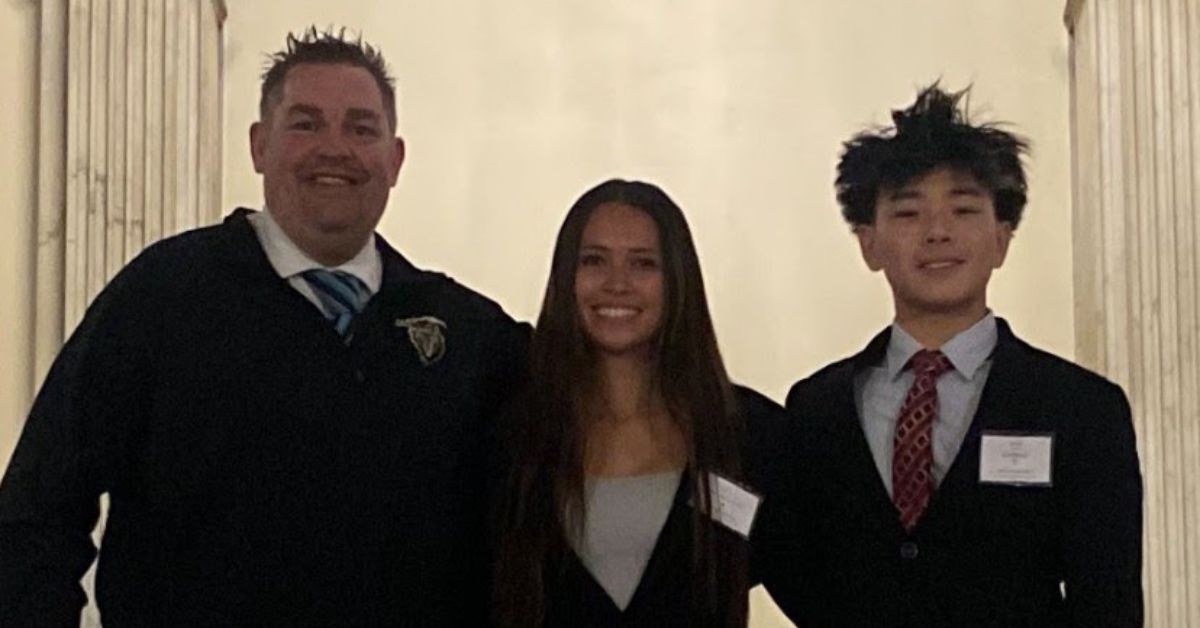 Nashoba Dean Ryan Wood stands with students Ava Wyman and Winston Zhao, all dressed in professional attire, smiling inside the Massachusetts State House during Student Government Day 2025.