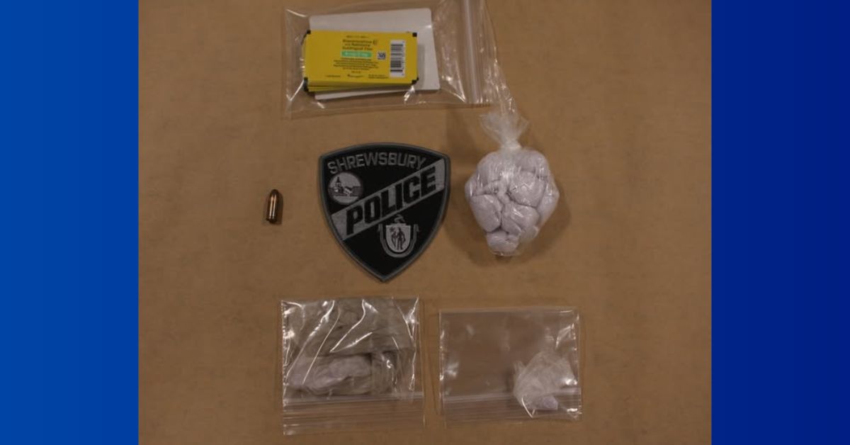 Evidence photo showing seized items arranged on a tan surface, including a single bullet, multiple plastic bags containing suspected drugs (fentanyl, cocaine, and buprenorphine), a yellow-labeled medication package, and a black Shrewsbury Police Department patch placed in the center.