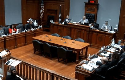 City councilors seated in chambers during the Worcester City Council meeting on April 1, 2025. Council members are spaced along a U-shaped desk, with the mayor and chairperson at the center podium, and others reviewing documents or listening to public comment. Screenshot from Worcester Meeting Video Archive.