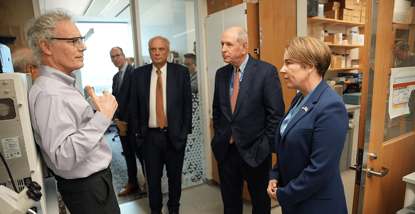 Victor R. Ambros, PhD, speaks to Governor Maura Healey, Chancellor Michael F. Collins, and Worcester Mayor Joseph M. Petty during a lab tour at the Paul J. DiMare Center, surrounded by lab equipment and observers.