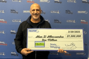 Alan D’Allessandro smiling and holding a large ceremonial check for $1 million from the Massachusetts State Lottery, dated March 20, 2025. Photo credit: Photo courtesy of the Massachusetts State Lottery