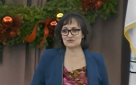 Mayor Katjana Ballantyne seated at her desk in City Hall, wearing a pink shirt and dark blazer, taking notes.​
