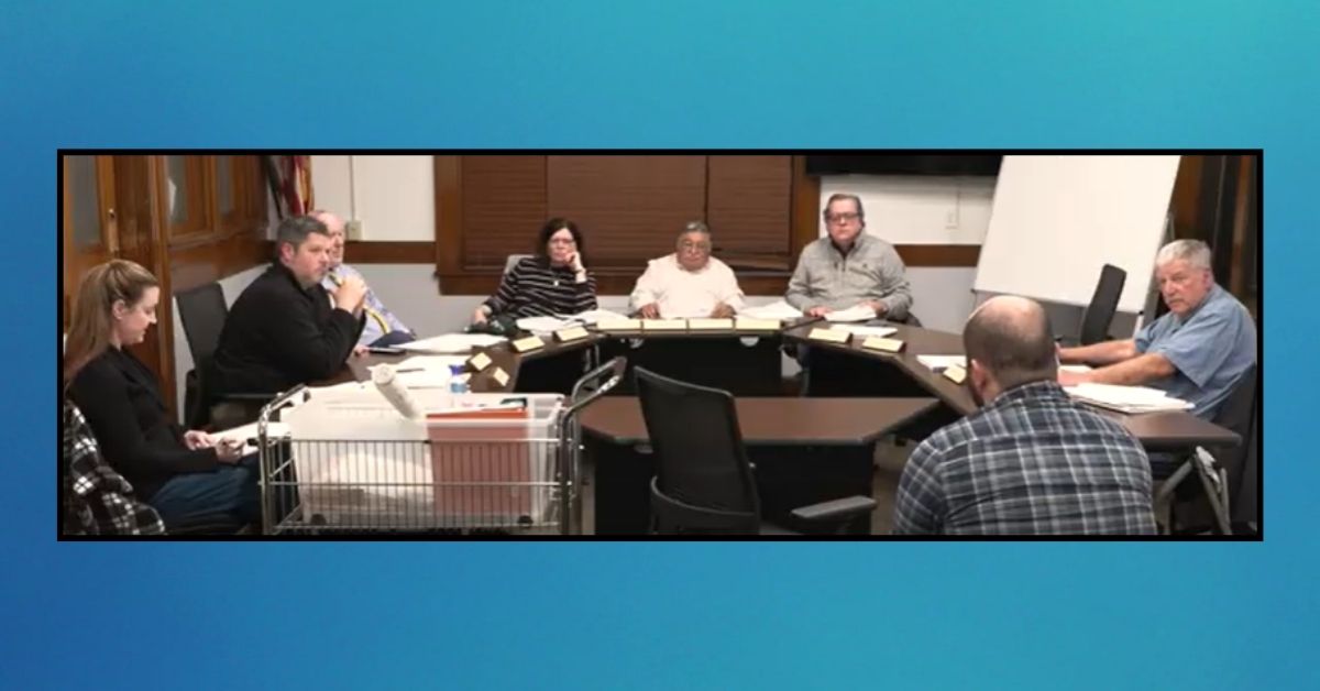 Leominster Planning Board members seated at a curved table listening during public comment at the May 5, 2025, meeting. A woman sits on the left with notes, and a man is seen from behind speaking to the board.