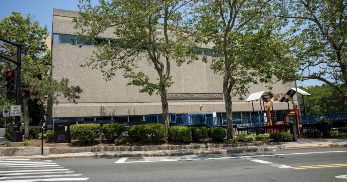 Exterior view of the Winter Hill Community Innovation School in Somerville, Massachusetts, with trees and a playground in front.