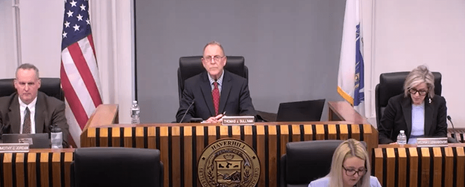 Haverhill City Council President Thomas J. Sullivan sits at the center of the council dais during a city council meeting, with Vice President Timothy J. Jordan on his left and Councilor Melissa Lewandowski on his right. An American flag and Massachusetts state flag are visible behind them.