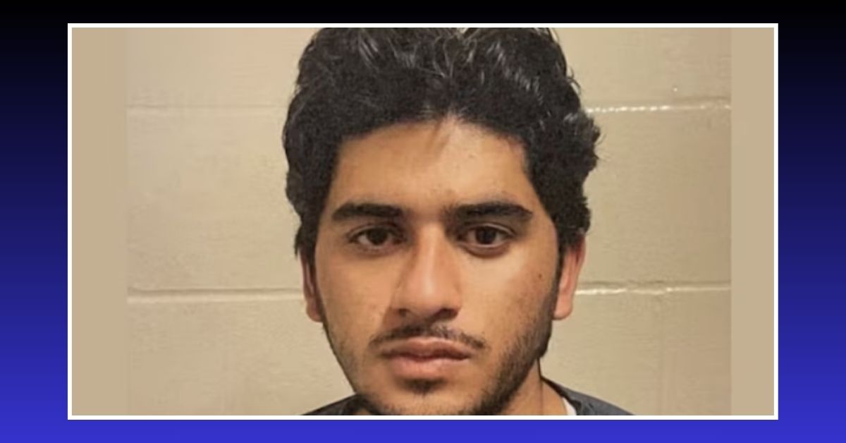 Mugshot of Muhammad Shahzeb Khan, a young man with dark hair and a trimmed beard, standing against a beige brick wall.