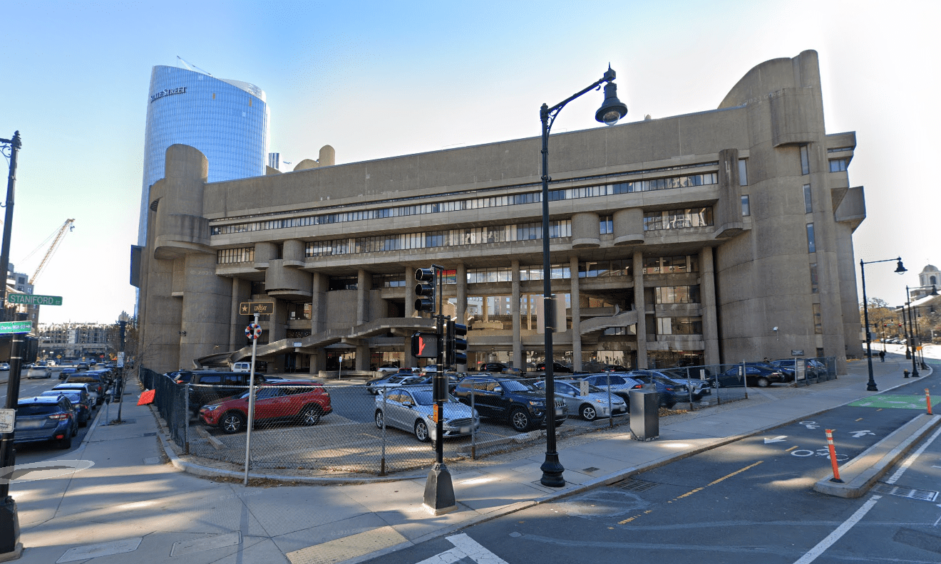 The Boston Government Service Center, a large Brutalist-style concrete building complex with a street-level parking lot, located at the corner of Staniford and Cambridge Streets in Boston.