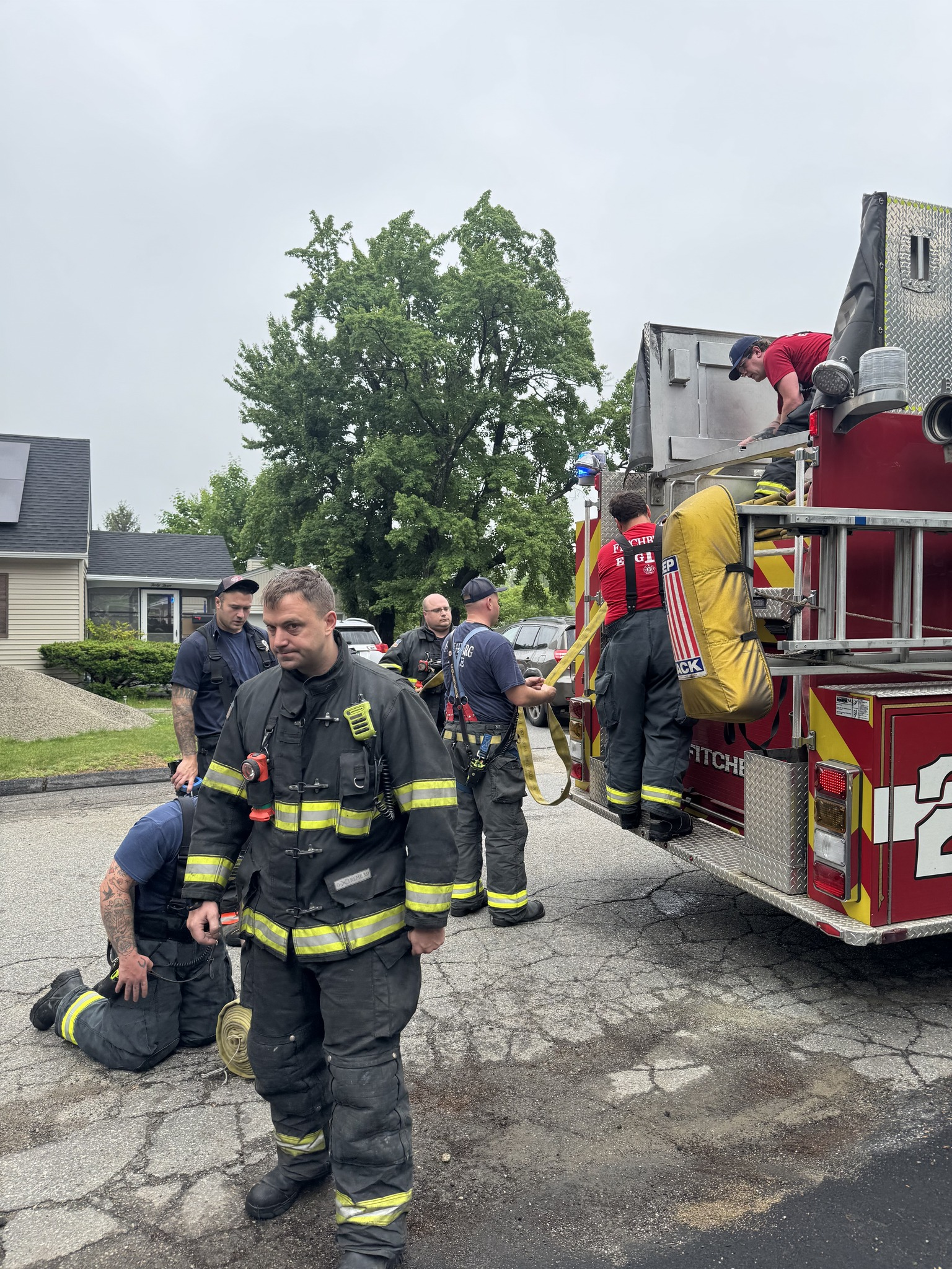 Firefighters gather on a residential street near a truck as they wrap up operations after a basement fire.