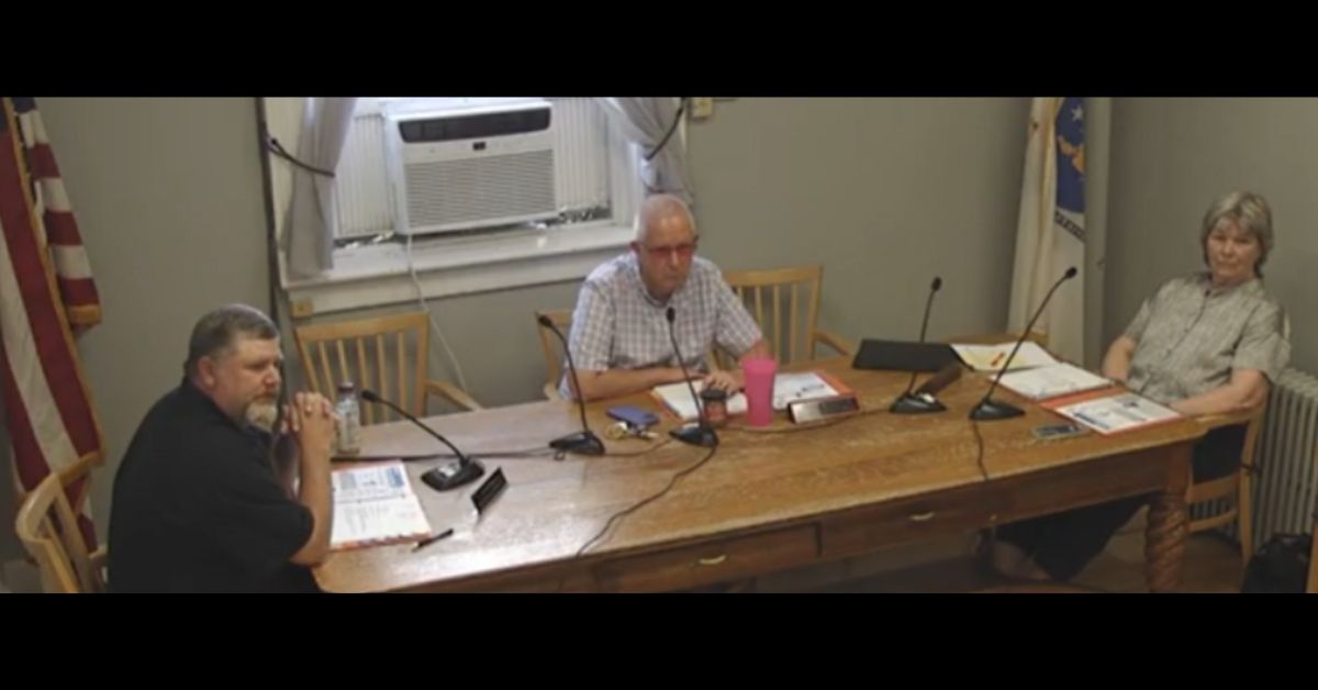 Three town officials seated at a wooden table during a meeting, discussing infrastructure issues.